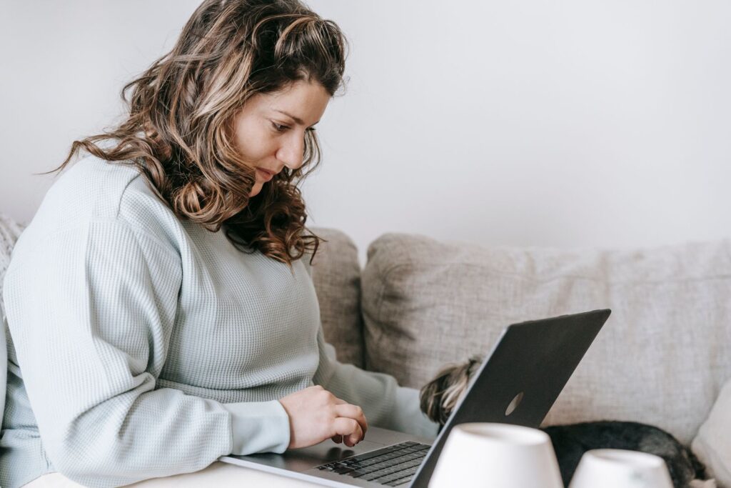 Woman working on a laptop while petting a dog at home